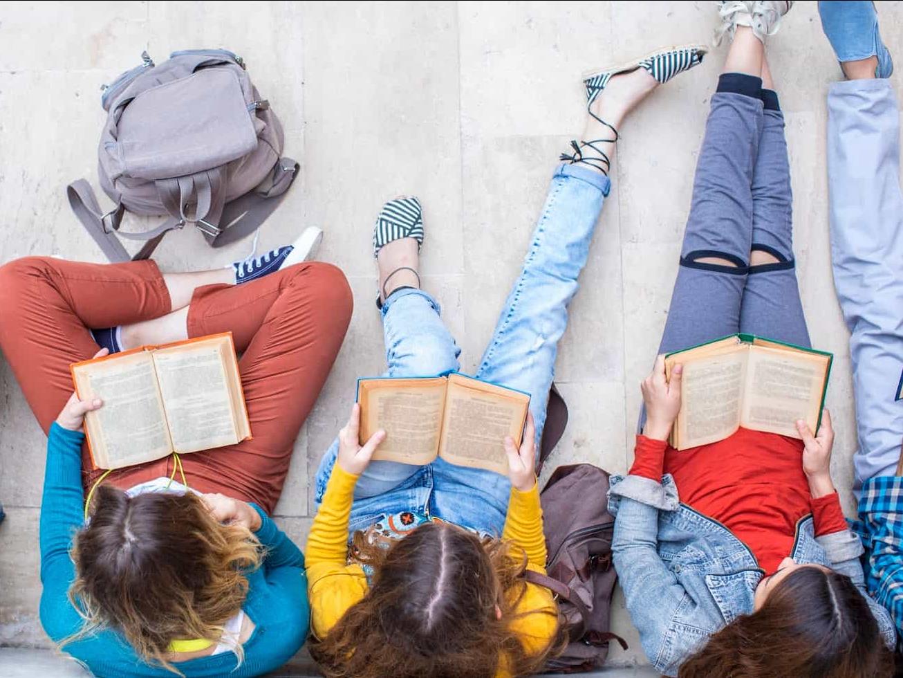 Teen students reading books on the floor. 